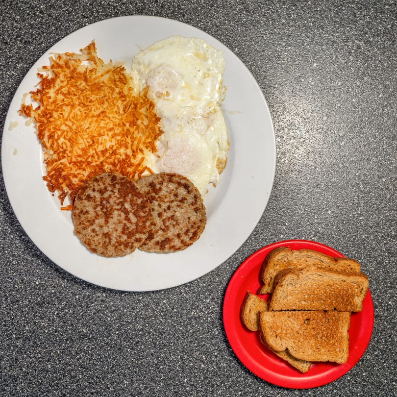 A diner breakfast with hash browns, two fried eggs, two sausage patties, and toast.